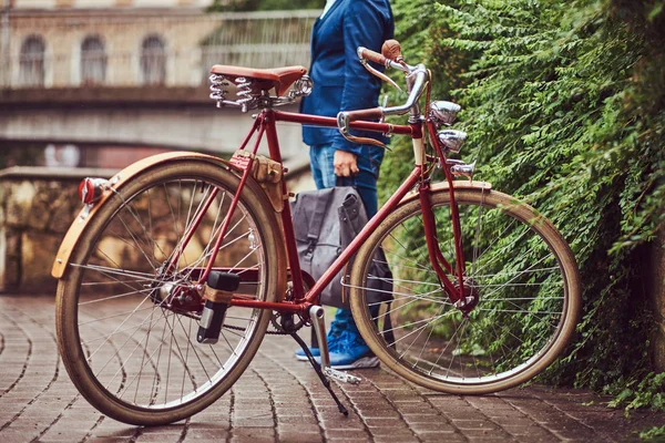 Homem vestido com roupas casuais, de pé perto de uma bicicleta retro em um parque . — Fotografia de Stock