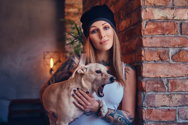 Blondynka tattoed stylowe kobiece w t-shirt i dżinsy posiada ładny pies. — Zdjęcie stockowe
