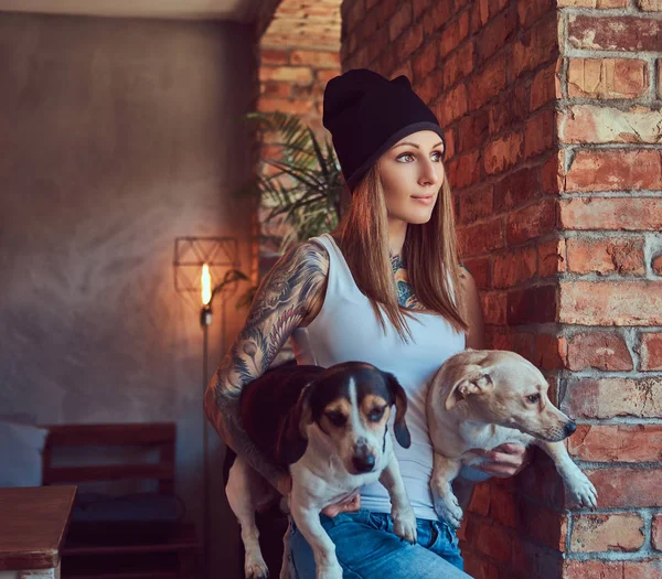 Blondynka tattoed stylowe kobiece w t-shirt i dżinsy posiada dwa psy. — Zdjęcie stockowe