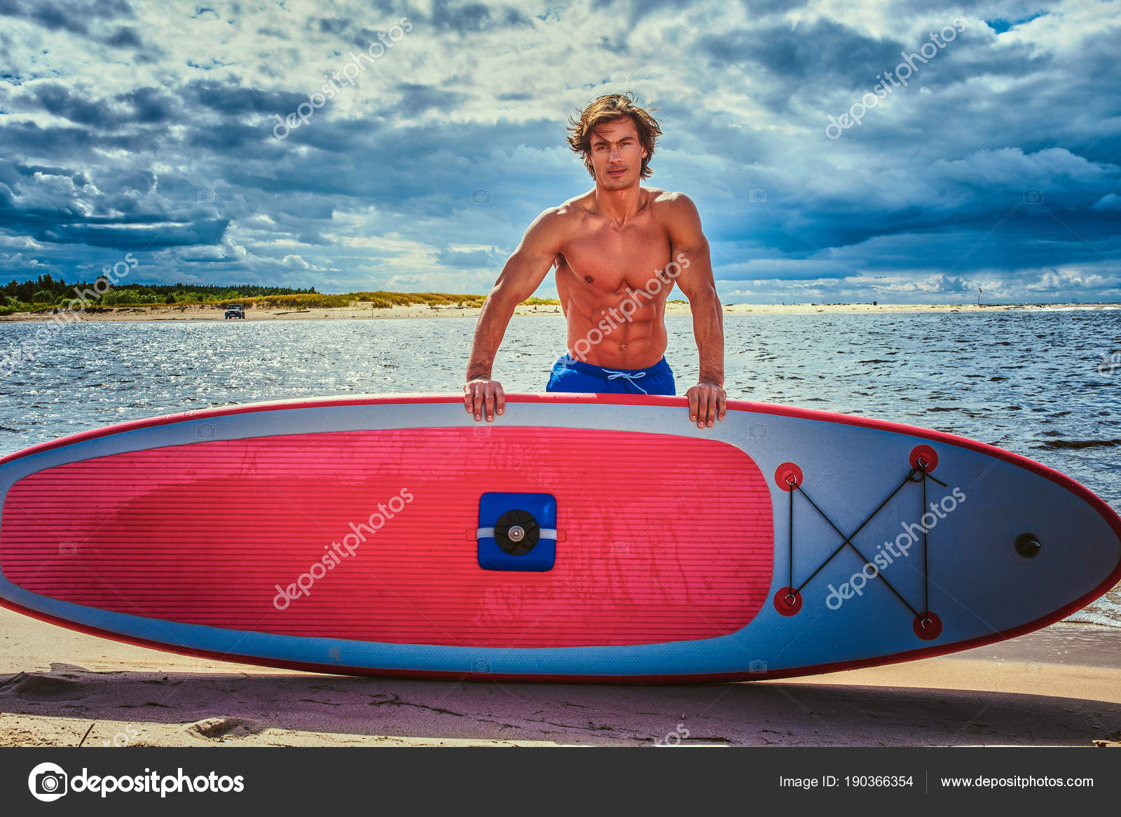 Surfer male with a muscular body with his surfboard at the beach. Stock