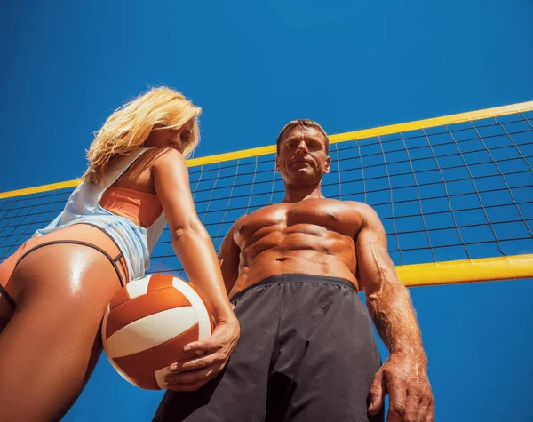 Couple sportif. Une belle fille blonde bronzée musclée masculine et sexy, debout sur un terrain de volley-ball . — Photo