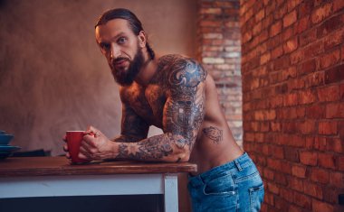 Yakışıklı sakallı tattoed erkek bir şık saç kesimi ve kas vücut, içecekler kahve, bir masanın üzerine eğilerek.