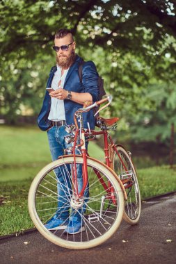 Bir gezgin rahat kıyafetler ve bir sırt çantası ile güneş gözlüğü giymiş bir smartphone kullanarak, bir şehir parkında bir retro binmek sonra rahatlatıcı.