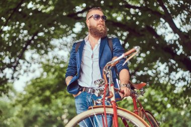 Rahat kıyafetler ve bir sırt çantası, rahatlatıcı bir retro bisiklet sürme sonra bir şehir parkı ile güneş gözlüğü Gezgin giymiş.