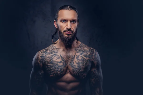 Close-up portret van een gespierde bebaarde tattoed man met een stijlvol kapsel, geïsoleerd op een donkere achtergrond. — Stockfoto