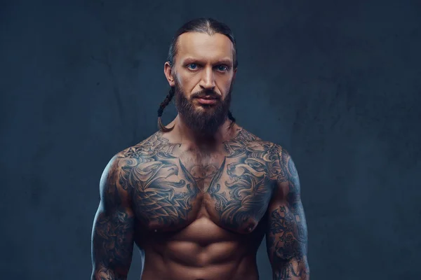 Close-up portrait of a muscular bearded tattoed male with a stylish haircut, isolated on a dark background. — Stock Photo, Image