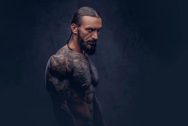 Ritratto ravvicinato di un maschio muscoloso tatuato barbuto con un taglio di capelli elegante, isolato su uno sfondo scuro . — Foto Stock