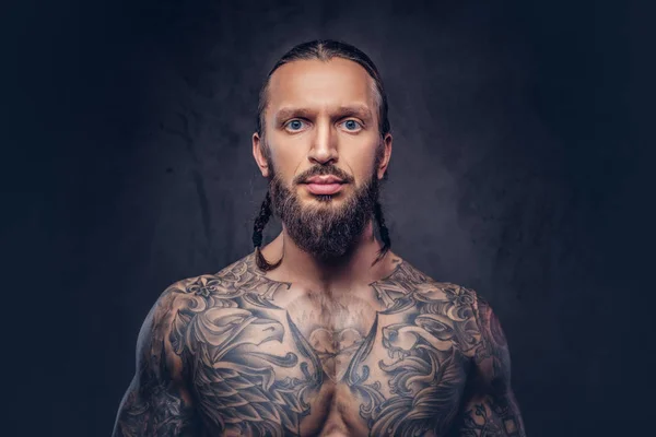 Close-up portret van een gespierde bebaarde tattoed man met een stijlvol kapsel, geïsoleerd op een donkere achtergrond. — Stockfoto