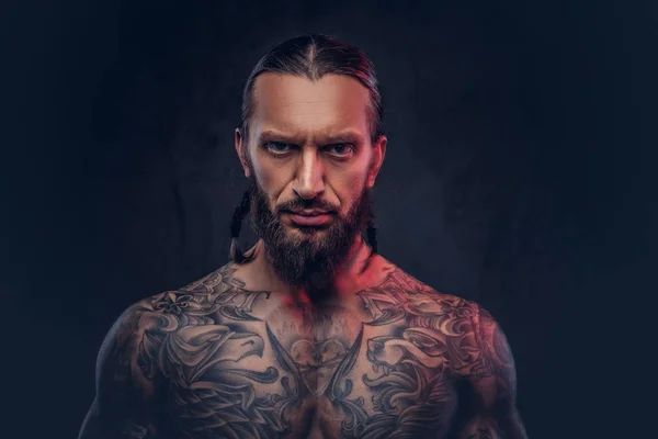 Close-up portret van een gespierde bebaarde tattoed man met een stijlvol kapsel, geïsoleerd op een donkere achtergrond. — Stockfoto