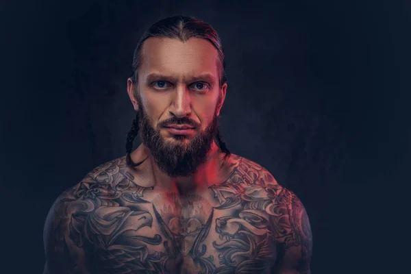 Close-up portrait of a muscular bearded tattoed male with a stylish haircut, isolated on a dark background. — Stock Photo, Image