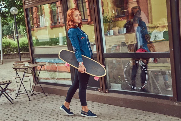 Молода руда дівчина зі скейтбордом, стоячи біля кав'ярні . — стокове фото