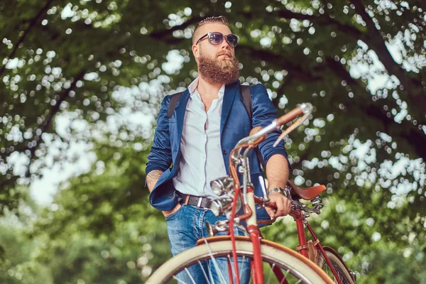 Reiziger gekleed in casual kleding en zonnebrillen met een rugzak, ontspannen in een stadspark na het rijden op een retro fiets. — Stockfoto