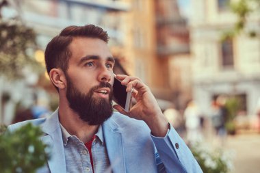 Telefonla konuşan moda sakallı işadamı şık bir saç kesimi ile yakın çekim portre bir kafe mekanlarda oturan bir suyu bir bardak içer.