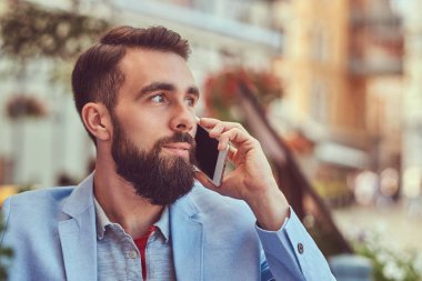 Telefonla konuşan moda sakallı işadamı şık bir saç kesimi ile yakın çekim portre bir kafe mekanlarda oturan bir suyu bir bardak içer.