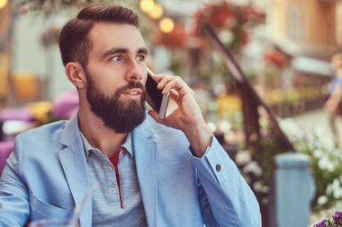 Telefonla konuşan moda sakallı işadamı şık bir saç kesimi ile yakın çekim portre bir kafe mekanlarda oturan bir suyu bir bardak içer.