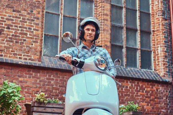 Hombre guapo con ropa casual en un casco, montado en un scooter clásico retro, a lo largo de las viejas calles de una Europa . —  Fotos de Stock