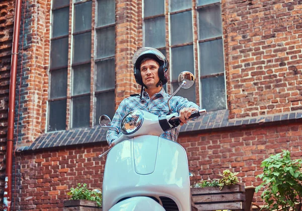 Hombre guapo con ropa casual en un casco, montado en un scooter clásico retro, a lo largo de las viejas calles de una Europa . — Foto de Stock