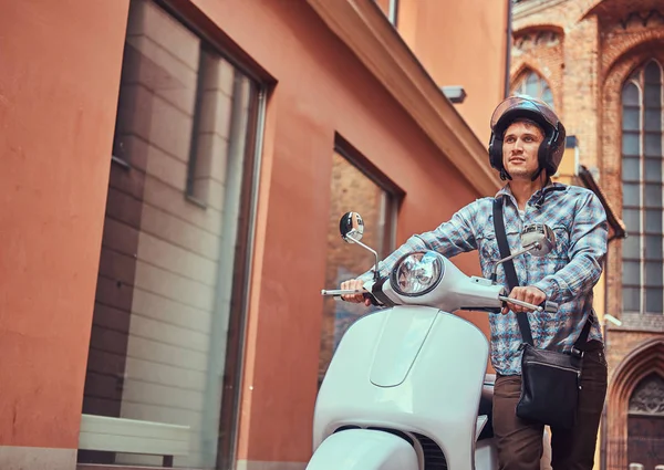 Hombre guapo con ropa casual en un casco, caminando por las viejas calles de una Europa con un scooter clásico retro . — Foto de Stock