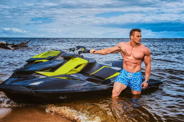 Beau sportif torse nu avec un corps musclé debout près du jet ski sur une côte . — Photo