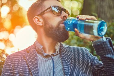 Açık havada soğuk su içiyor, bir şehir parkta bir bankta oturan erkek sakallı.