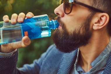 Açık havada soğuk su içiyor, bir şehir parkta bir bankta oturan erkek sakallı.