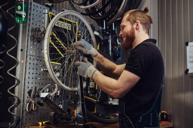 Bir bisiklet tekerleği bir tamir dükkanında çalışan yakışıklı Kızıl saçlı erkek kot pantolon coverall içinde. Bir işçi Bisiklet lastik bir atölyede kaldırır..