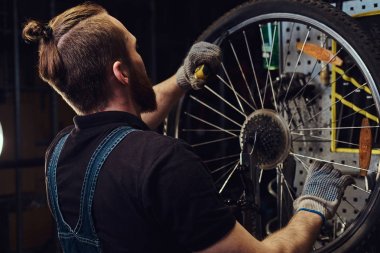 Bir bisiklet tekerleği bir tamir dükkanında çalışan yakışıklı Kızıl saçlı erkek kot pantolon coverall içinde. Bir işçi Bisiklet lastik bir atölyede kaldırır..