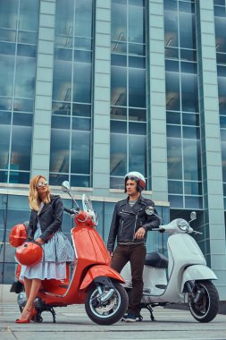 Çekici Romantik Çift, yakışıklı ve seksi erkek, bir gökdelen karşı iki retro İtalyan scooter ile ayakta.