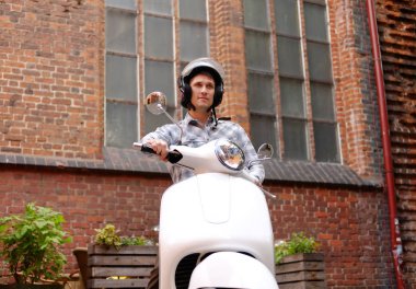 Yakışıklı adam bir kask, rahat kıyafetler giymiş bir Avrupa'nın eski sokaklar boyunca retro bir klasik scooter sürme.