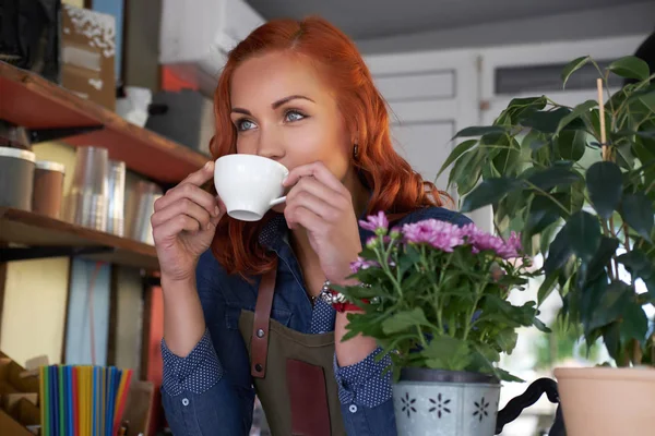 Eine rothaarige Barista trinkt einen Kaffee im Café. — Stockfoto