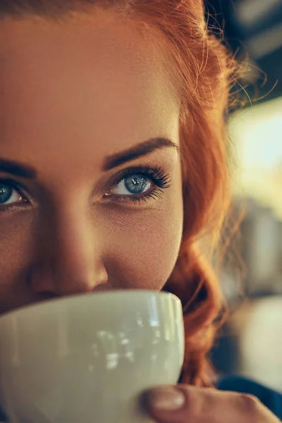 A beauty redhead female barista drinks a coffee, at the coffee shop.