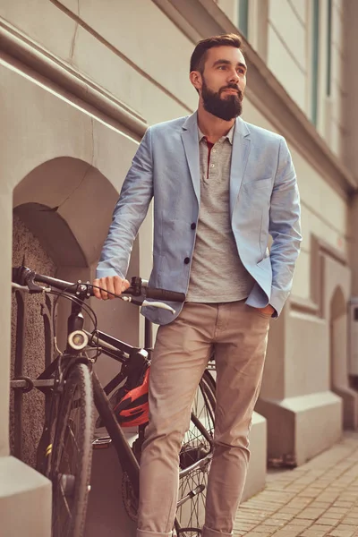 おしゃれなひげを生やした男性の身に着けているスタイリッシュな服、アンティークのヨーロッパの通りの自転車スタンド. — ストック写真