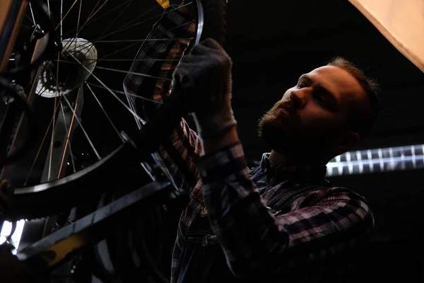 Przystojny stylowy mężczyzna sobie Flanelowa koszula i jeansy kombinezon, praca z koła rowerowego w warsztacie. — Zdjęcie stockowe
