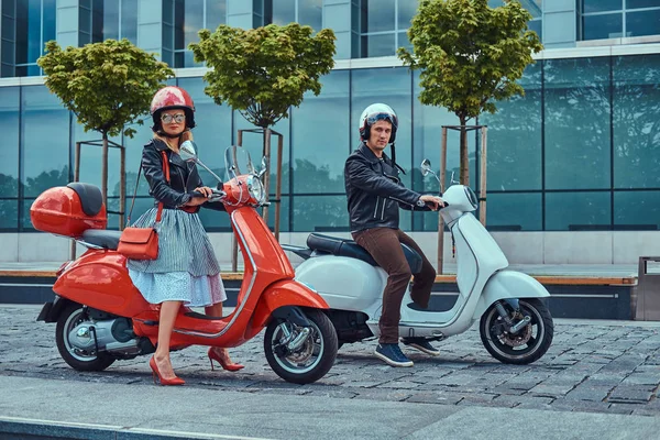 Atractiva pareja romántica, un hombre guapo y sexy hembra, sentado en scooters italianos retro contra un rascacielos . —  Fotos de Stock