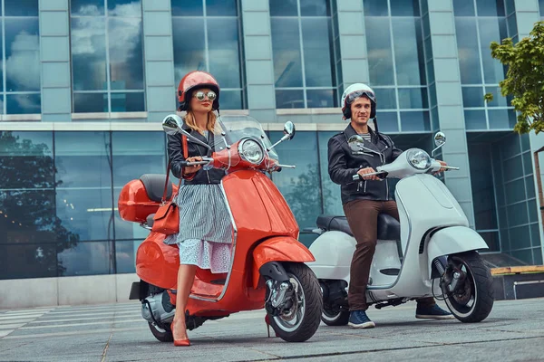 Aantrekkelijke romantisch paar, een knappe man en sexy vrouw, permanent met twee retro Italiaanse scooters tegen een wolkenkrabber. — Stockfoto