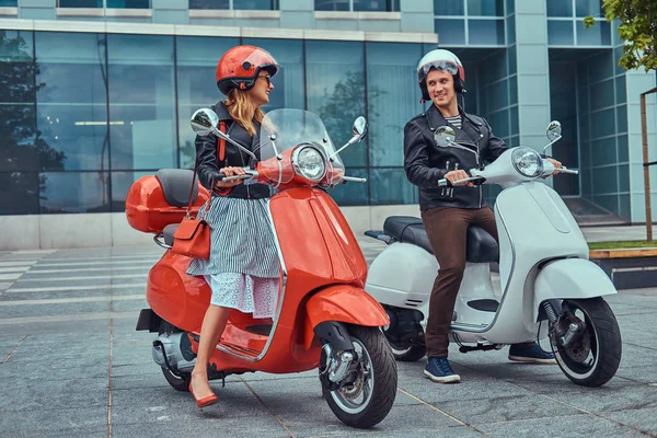 Aantrekkelijke romantisch paar, een knappe man en sexy vrouw, permanent met twee retro Italiaanse scooters tegen een wolkenkrabber. — Stockfoto