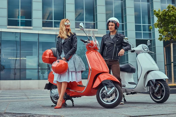 Aantrekkelijke romantisch paar, een knappe man en sexy vrouw, permanent met twee retro Italiaanse scooters tegen een wolkenkrabber. — Stockfoto