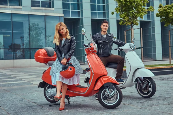 Attraktives romantisches Paar, ein gutaussehender Mann und eine sexy Frau, die mit zwei italienischen Retro-Rollern vor einem Wolkenkratzer steht. — Stockfoto