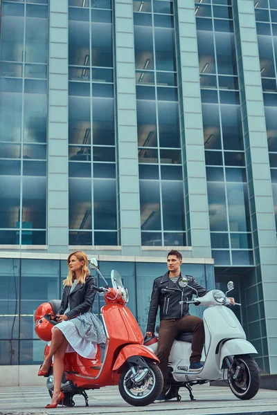 Attraktiva romantiska par och en stilig man som sexig kvinna, stående med två retro italienska skotrar mot en skyskrapa. — Stockfoto