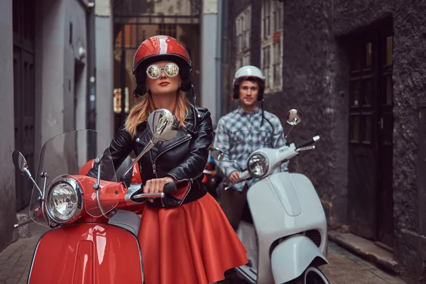 Schöner Mann und ein sexy stylisches Mädchen spazieren mit italienischen Retro-Rollern durch die alten Straßen der Stadt. — Stockfoto