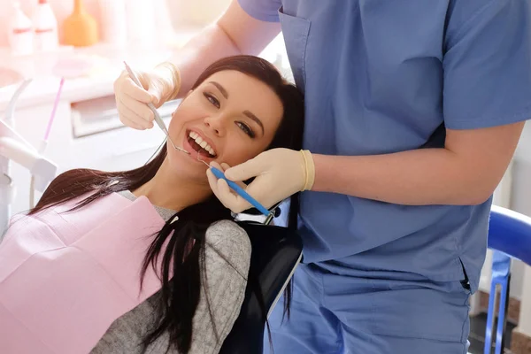 Dentista en uniforme azul y guantes blancos se preocupa por una sexy morena caucásica mujer, de pie detrás de ella . —  Fotos de Stock