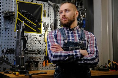 Sakal ve saç kesimi çapraz kollarında bir atölye ile ayakta bir pazen tişört ve kot coverall, giymiş yakışıklı şık erkek portresi.