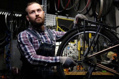 Bir bisiklet tekerleği bir tamir dükkanında çalışan bir fanila coverall, tişört ve kot giyen bir yakışıklı şık erkek. Bir işçi bir anahtarı kullanarak bir atölyede bisikletle tekerlek bağlar.