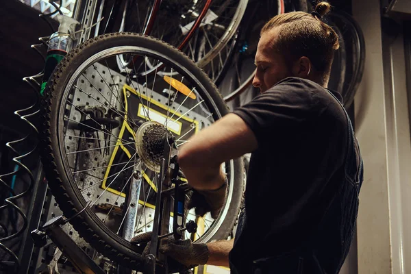 Красивый Рыжий Мужчина Джинсовом Комбинезоне Работающий Велосипедным Колесом Мастерской Рабочий — стоковое фото