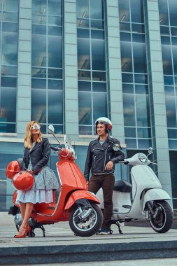 Çekici bir romantik çift, yakışıklı ve seksi erkek, bir gökdelen karşı iki retro İtalyan scooter ile ayakta.