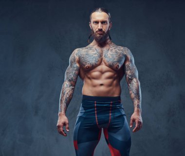Bir kaslı çıplak sakallı dövmeli erkek spor pantolon şık bir saç kesimi ile portresi. Karanlık bir arka plan üzerinde izole.