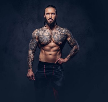 Bir kaslı çıplak sakallı dövmeli erkek spor pantolon şık bir saç kesimi ile portresi. Karanlık bir arka plan üzerinde izole.
