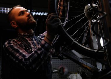 Bir bisiklet tekerleği bir tamir dükkanında çalışan bir fanila coverall, tişört ve kot giyen bir yakışıklı şık erkek.