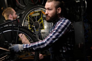 Bir bisiklet tamir dükkanında çalışan iki yakışıklı şık erkek. İşçi onarmak ve bisiklet bir atölyede bağlar.
