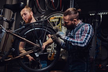 Bir bisiklet tamir dükkanında çalışan iki yakışıklı şık erkek. İşçi onarmak ve bisiklet bir atölyede bağlar.